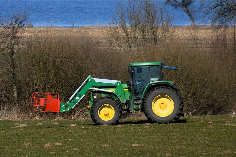 A green tractor loader driving on a green grass field