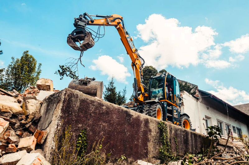a backhoe lifting a tree branch in front of a home renovation project