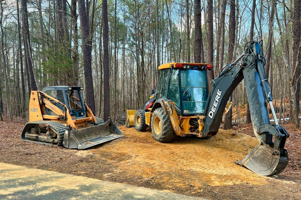 Skid steer and backhoe in woods